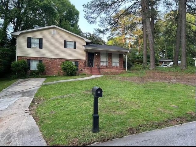 split level home with concrete driveway, a porch, brick siding, and a front lawn