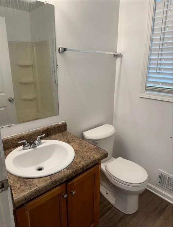 full bathroom with toilet, a shower, wood finished floors, vanity, and visible vents