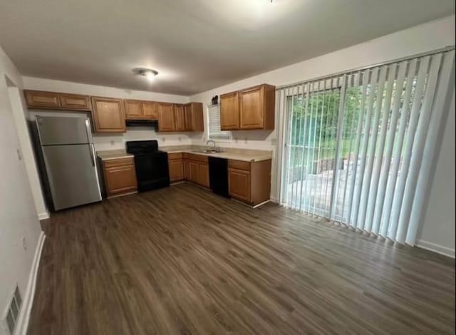kitchen with a sink, dark wood-style flooring, light countertops, and black appliances