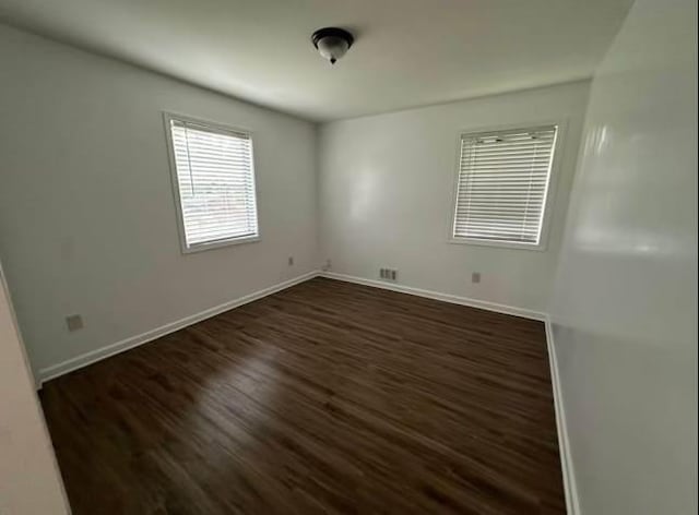 unfurnished room with baseboards and dark wood-type flooring
