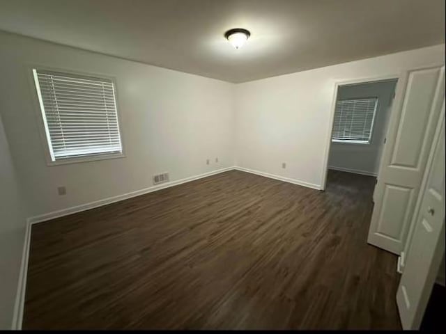 unfurnished room with baseboards, visible vents, and dark wood finished floors