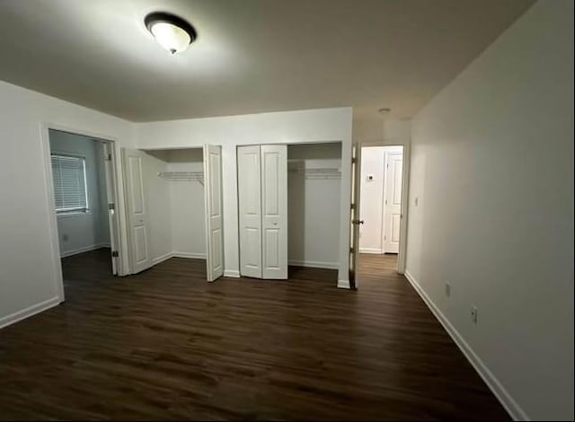 unfurnished bedroom featuring baseboards, multiple closets, and dark wood finished floors