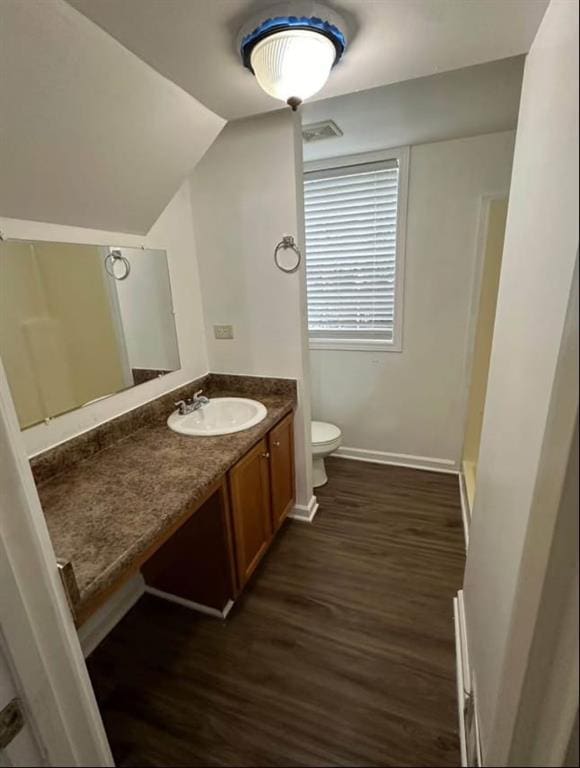bathroom with toilet, lofted ceiling, wood finished floors, vanity, and baseboards