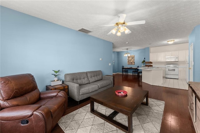 living area featuring light wood finished floors, visible vents, a textured ceiling, and a ceiling fan