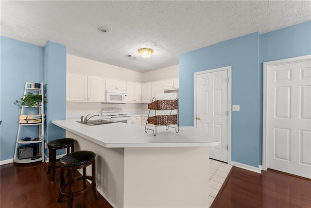 kitchen featuring white appliances, wood finished floors, a sink, light countertops, and a kitchen bar