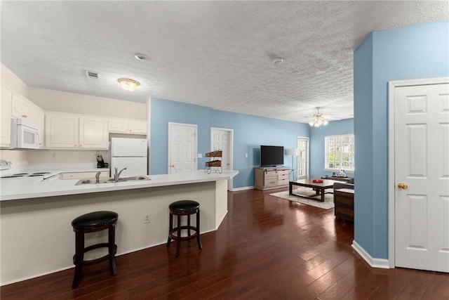 kitchen featuring white appliances, visible vents, dark wood finished floors, a peninsula, and a kitchen breakfast bar