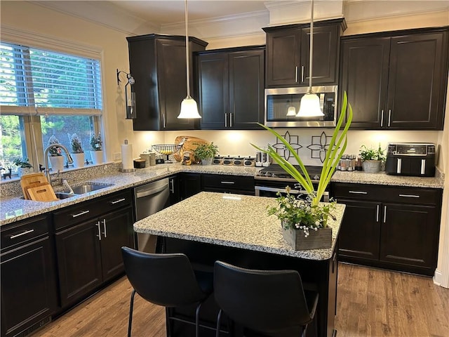 kitchen with appliances with stainless steel finishes, sink, a kitchen bar, hanging light fixtures, and ornamental molding