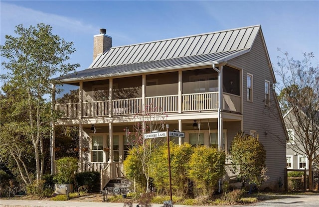 rear view of property featuring ceiling fan, a chimney, and a standing seam roof