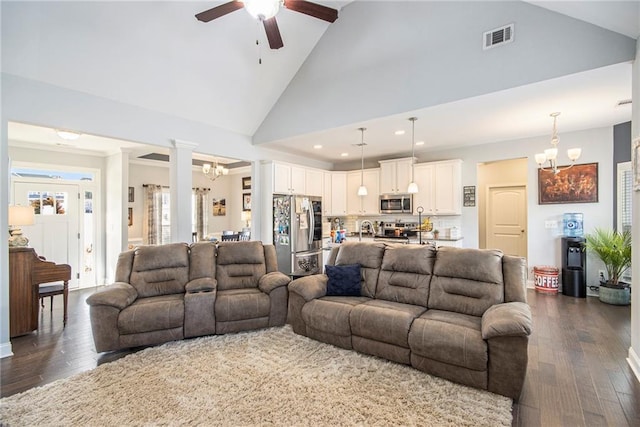 living room with ceiling fan with notable chandelier, high vaulted ceiling, dark hardwood / wood-style floors, and decorative columns