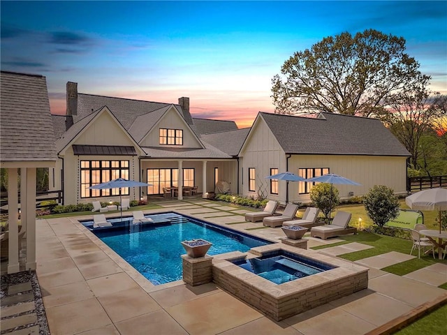 back house at dusk with a swimming pool with hot tub and a patio