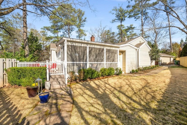 rear view of house featuring a garage, a chimney, fence, and a sunroom