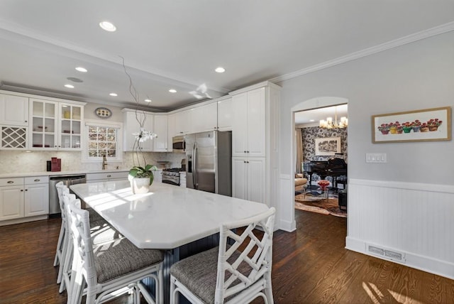 kitchen featuring dark wood-style floors, arched walkways, a wainscoted wall, appliances with stainless steel finishes, and white cabinetry