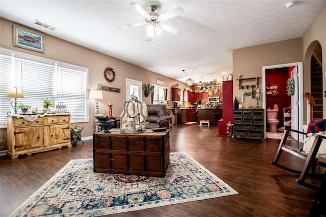 living area featuring arched walkways, visible vents, dark wood-type flooring, ceiling fan, and a textured ceiling