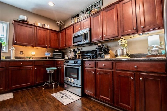 kitchen featuring a toaster, appliances with stainless steel finishes, dark wood finished floors, and dark stone countertops