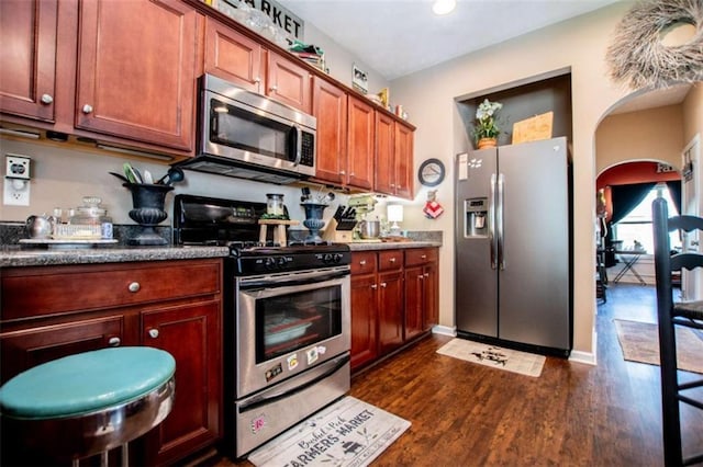 kitchen featuring arched walkways, appliances with stainless steel finishes, and dark wood finished floors