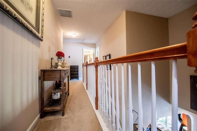 corridor featuring light carpet, baseboards, visible vents, and attic access