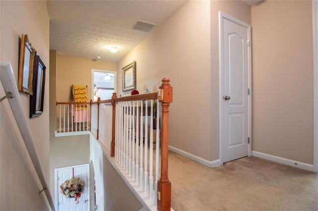 hall with baseboards, visible vents, an upstairs landing, a textured ceiling, and carpet flooring