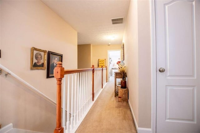 hallway with light carpet, baseboards, visible vents, and an upstairs landing