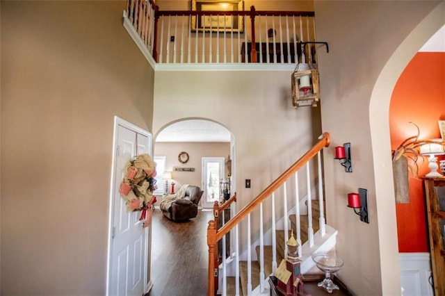 staircase with arched walkways, a high ceiling, and wood finished floors