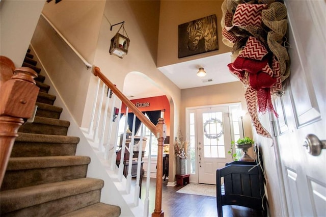 entrance foyer with arched walkways, stairway, wood finished floors, and visible vents