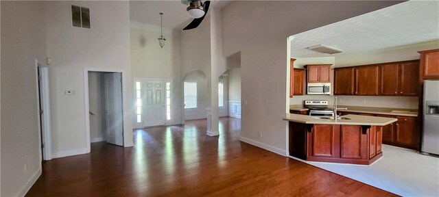 kitchen with sink, a towering ceiling, stainless steel appliances, wood-type flooring, and an island with sink