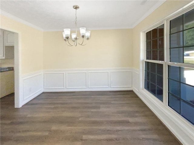 unfurnished dining area with ornamental molding, dark wood finished floors, a wainscoted wall, and a notable chandelier