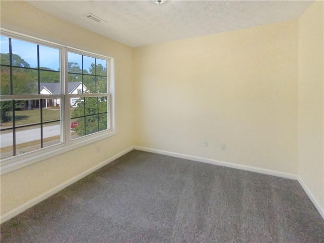 spare room featuring dark colored carpet, visible vents, and baseboards