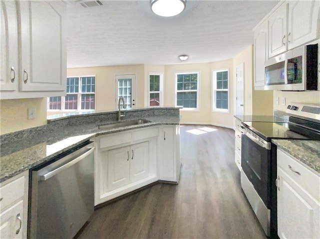 kitchen with stainless steel appliances, dark wood-type flooring, white cabinetry, a sink, and a peninsula