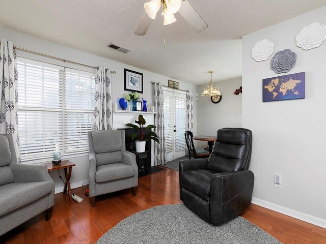 sitting room featuring ceiling fan with notable chandelier, a healthy amount of sunlight, a textured ceiling, and dark hardwood / wood-style floors