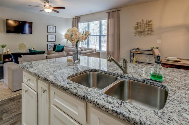 kitchen featuring dark wood finished floors, light stone counters, open floor plan, white cabinetry, and a sink