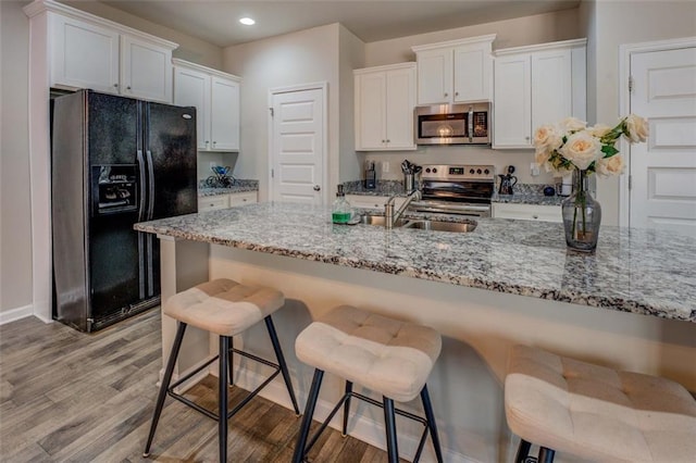 kitchen with light wood finished floors, white cabinets, stainless steel appliances, a kitchen bar, and a sink