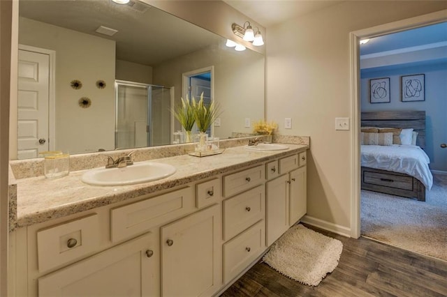 full bathroom featuring double vanity, a shower stall, a sink, and wood finished floors