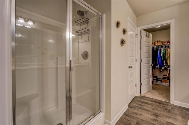 full bathroom with wood finished floors, a shower stall, a walk in closet, and baseboards