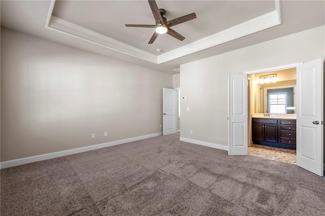 unfurnished bedroom with sink, crown molding, ensuite bath, a tray ceiling, and light colored carpet