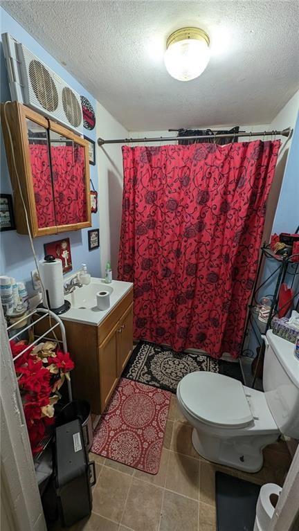 bathroom featuring a textured ceiling, a shower with shower curtain, tile patterned floors, vanity, and toilet