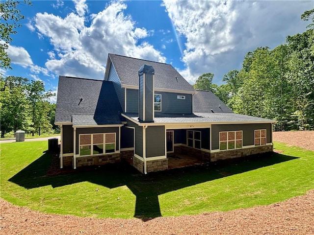 back of house featuring a yard, stone siding, and a shingled roof