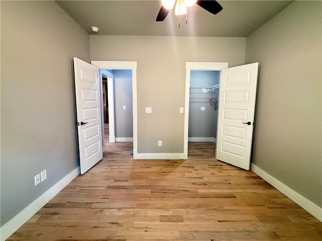 unfurnished bedroom with a closet, a ceiling fan, a walk in closet, baseboards, and light wood-style floors
