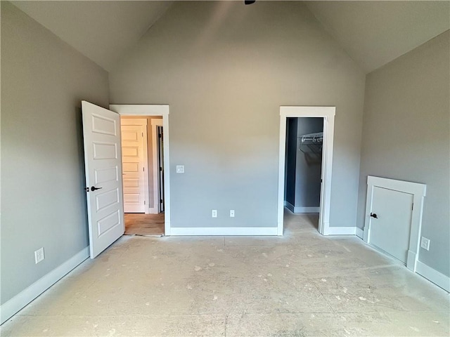 unfurnished bedroom with a walk in closet, baseboards, high vaulted ceiling, and a closet