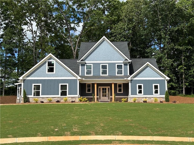 craftsman-style house featuring a porch, a shingled roof, stone siding, and a front yard
