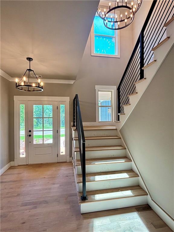 foyer entrance with light wood-style floors, stairway, a healthy amount of sunlight, and a notable chandelier