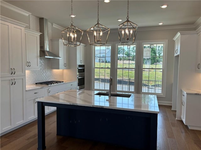 kitchen featuring pendant lighting, sink, white cabinets, a center island with sink, and wall chimney exhaust hood