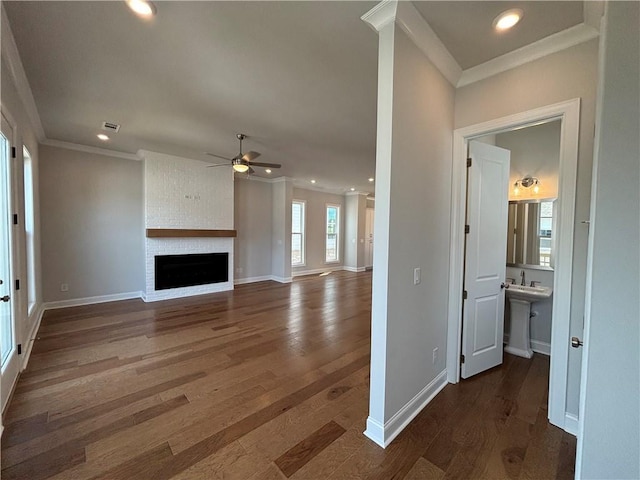 unfurnished living room featuring crown molding, ceiling fan, a fireplace, and dark wood-type flooring