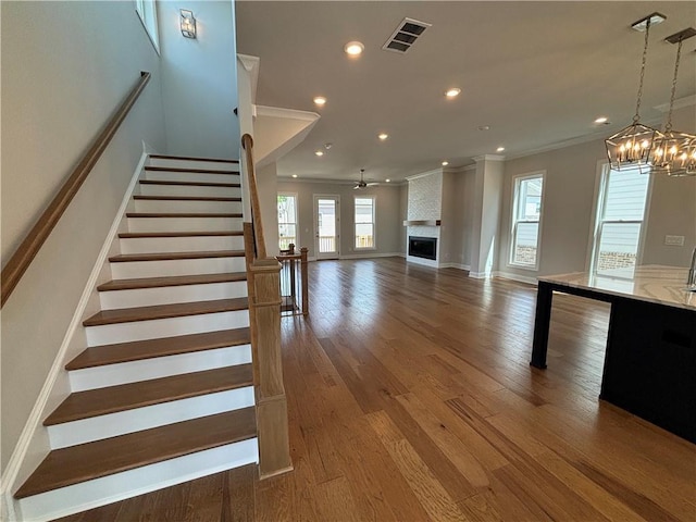 staircase featuring crown molding, a large fireplace, hardwood / wood-style floors, and ceiling fan