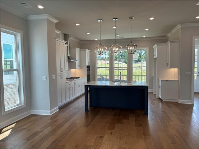 kitchen featuring an island with sink, sink, white cabinets, hanging light fixtures, and crown molding