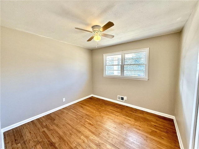 spare room with visible vents, wood finished floors, a ceiling fan, and baseboards