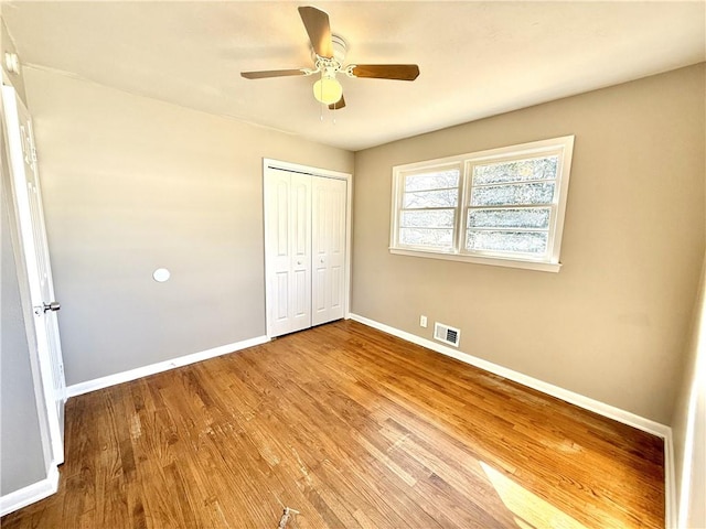 unfurnished bedroom featuring a closet, visible vents, ceiling fan, wood finished floors, and baseboards