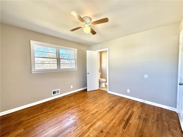 unfurnished bedroom with baseboards, visible vents, a ceiling fan, wood finished floors, and ensuite bathroom