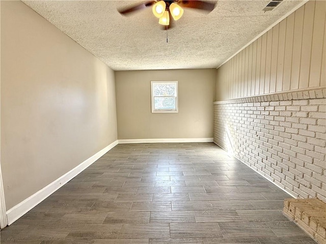 unfurnished room with dark wood-type flooring, a ceiling fan, a textured ceiling, brick wall, and baseboards