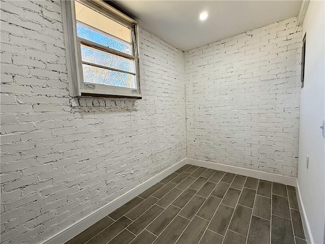 empty room with baseboards, brick wall, and wood tiled floor