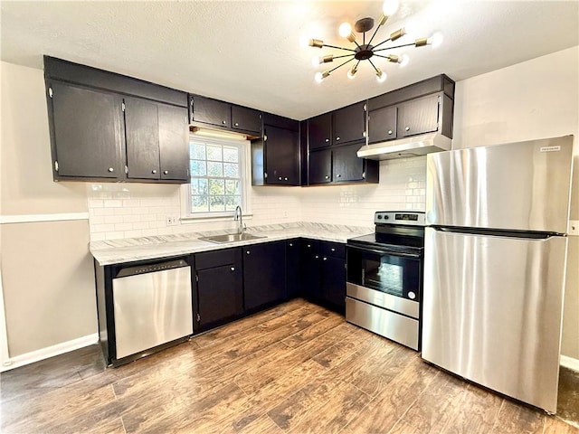 kitchen featuring decorative backsplash, appliances with stainless steel finishes, a sink, wood finished floors, and under cabinet range hood